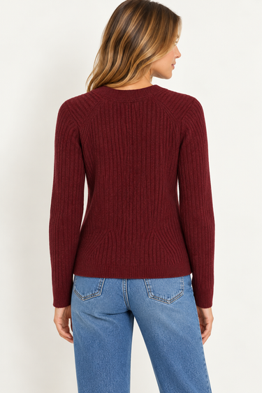 a woman wearing a burgundy ribbed v-neck cardigan and blue jeans on a white background.