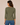 A woman viewed from the back wearing a fitted olive green three-quarter sleeve top and blue jeans against a plain beige studio background.