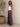 Woman wearing a white tank top and patterned pants standing next to a potted plant.
