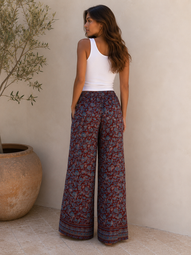 Woman wearing a white tank top and patterned wide-leg pants standing against a neutral wall.