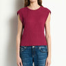 A woman wearing a ribbed knit sleeveless top in deep burgundy and blue jeans, standing against a plain off-white wall.