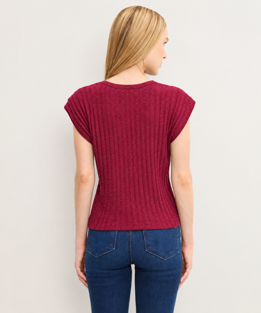 A woman shown from the back wearing a ribbed short-sleeve top in deep burgundy and blue jeans, standing against a plain light gray background.