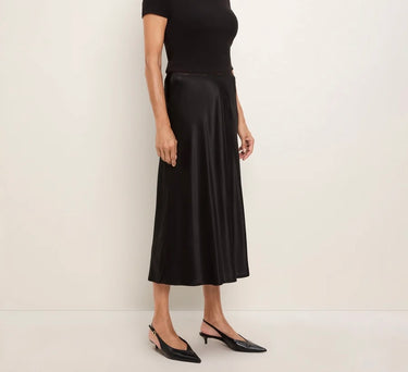 a woman wearing a black tee and a black bias midi skirt on a white background.