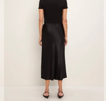a woman wearing a black tee and a black bias midi skirt on a white background.