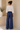 Woman wearing a white blouse and blue pants standing in a minimalistic room with a plant.