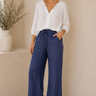 Woman wearing a white blouse and blue pants standing against a beige wall.
