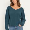 A woman wearing a teal ribbed long sleeve top and blue jeans on a white background.