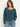 A woman wearing a teal ribbed long sleeve top and blue jeans on a white background.