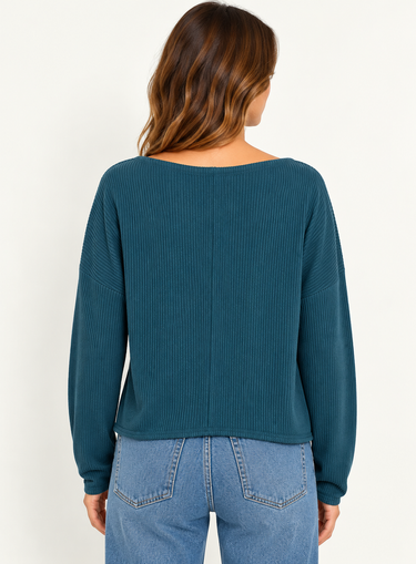 A woman wearing a teal ribbed long sleeve top and blue jeans on a white background.