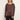A woman wearing a long-sleeve, boat-neck top in a dark brown color, paired with black pants, standing against a plain off-white background.