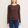 A woman wearing a ribbed long-sleeve crewneck sweater in a dark brownish-purple color, paired with blue jeans, against a plain light background.