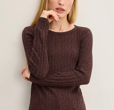 A woman wearing a dark brown ribbed long-sleeve knit top, shown from the chin down against a plain light gray background.