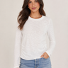 A woman modeling a white long-sleeve crewneck top with side ruching, paired with light blue jeans, against a plain light beige studio background.