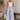 Woman wearing a white tank top and light blue pants, holding a woven bag indoors.