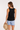 Woman wearing a black sleeveless top and denim shorts, holding a straw hat on a white background