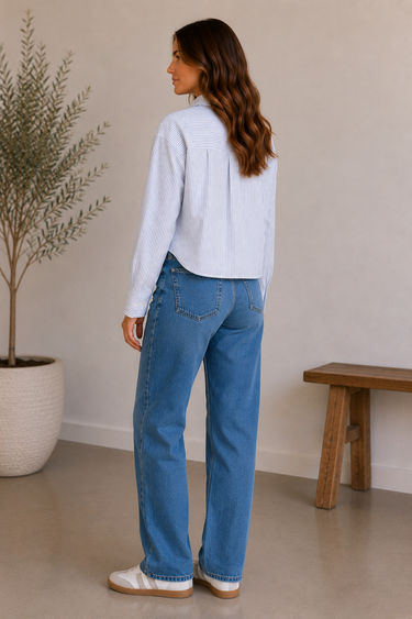 Woman wearing a light blue sweater and jeans standing in a room with a plant and wooden bench.