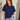 Woman wearing a blue t-shirt and denim shorts indoors.