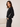 A woman wearing a black cropped sweatshirt with white stripes on the sleeves, paired with black jeans, standing in a studio setting.
