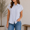 Woman wearing a blue and white striped shirt and jeans standing in a room with a plant and wooden bench.