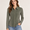 A woman modeling a long-sleeve button-up shirt in olive green, paired with blue jeans, against a plain light beige studio background.
