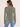 A woman shown from the back wearing a long-sleeve collared blouse in a muted sage green color, paired with light blue jeans, against a plain off-white studio background.