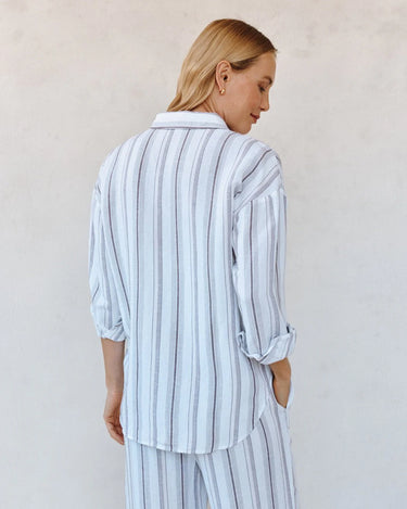 Woman wearing a light blue and white striped pajama set against a plain background