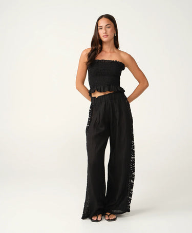 A woman wearing black pants with a side lace panel and a black tube top.