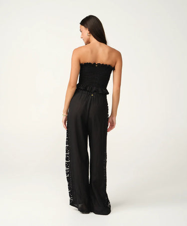 A woman wearing black pants with a side lace panel and a black tube top.