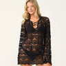 A model wearing a black bikini under a black lace long-sleeve tunic cover-up with scalloped pattern, lace-up V-neck and tassel ties.