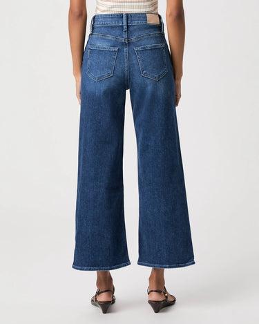 A model shown from the back wearing dark blue wide-leg cropped denim jeans, a striped top, and black sandals against a plain light gray studio background.
