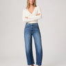 Woman wearing a white sweater and blue jeans on a plain background
