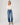 Woman wearing a white sweater and blue jeans on a plain background