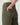 Close-up of a person wearing olive green wide-leg pants, showing the back pocket and hand in the pocket, paired with a white ribbed top against a light gray background.