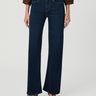 A model wearing dark blue wide-leg flare jeans, paired with a brown blouse and brown wedge sandals, shown from the waist down on a light gray studio background.