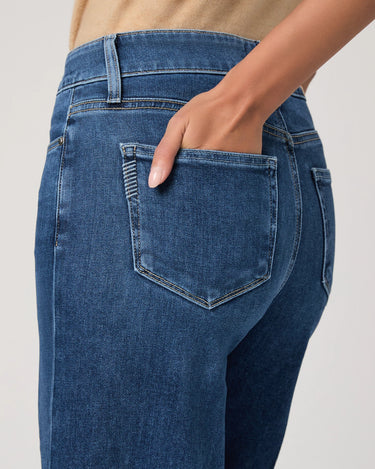 Close-up of blue jeans with a hand in the pocket against a neutral background