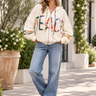 A woman wearing  oversized white jacket with “Peace” written across the front and Blue jeans on Outside background 