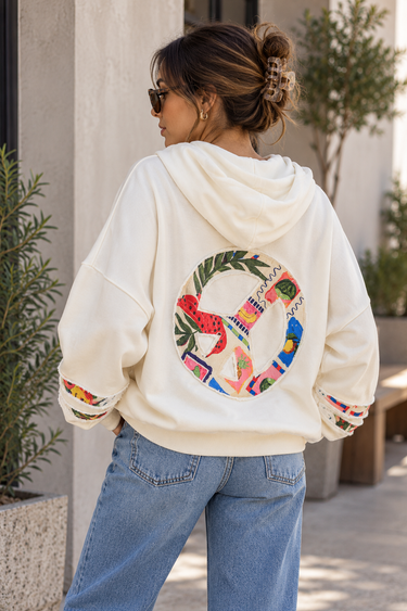 a woman wearing a white oversized hoodie with a colorful peace sign on the back