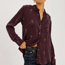 a woman wearing a burgundy blouse with Martin glasses printed on and dark blue denim on a white background.