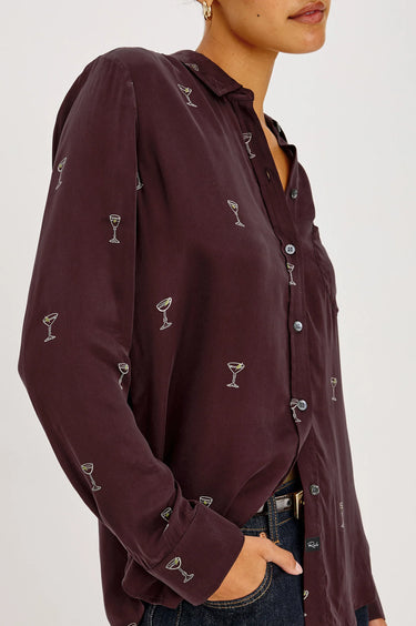 a woman wearing a burgundy blouse with Martin glasses printed on and dark blue denim on a white background.