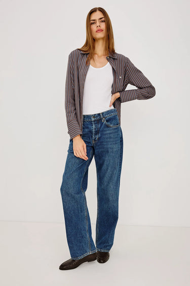 Woman wearing a striped shirt, white top, and blue jeans on a light gray background