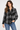 a woman wearing a black and ivory plaid collared shirt and blue jeans on a white background.