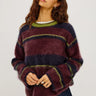 A woman wearing a burgundy, navy and green stripe brushed wool crew neck sweater and dark blue denim jeans on a white background 