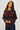 A woman wearing a burgundy, navy and green stripe brushed wool crew neck sweater and dark blue denim jeans on a white background 