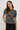 A woman wearing a short sleeve charcoal sweater with velvet black bows and a black midi skirt on a white background.