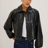 A woman wearing a black faux leather jacket, a white tee,  and dark blue denim on a white background.