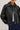 A woman wearing a black faux leather jacket, a white tee,  and dark blue denim on a white background.