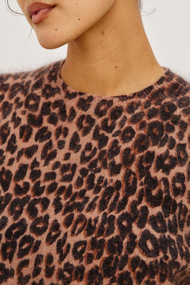 Close-up of a person wearing a fuzzy knit top with a leopard print pattern in brown and black on a dusty pink background.