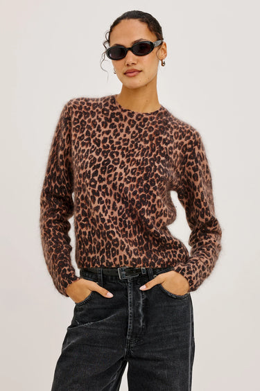 Person wearing a leopard print sweater and black pants on a plain background