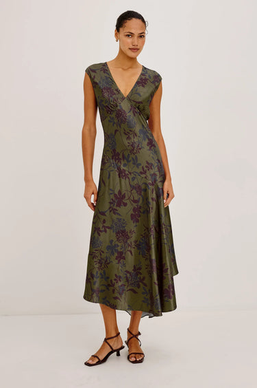 A woman wearing a v-neck sleeveless, floral  midi dress with an asymmetrical skirt and burgundy heels on a white background.