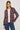A woman modeling a long-sleeve button-up plaid shirt in burgundy, gray, and white, worn open over a white t-shirt and blue jeans, against a light gray studio background.